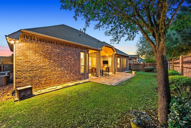 back of house at dusk with brick siding, a shingled roof, a patio, and central AC unit