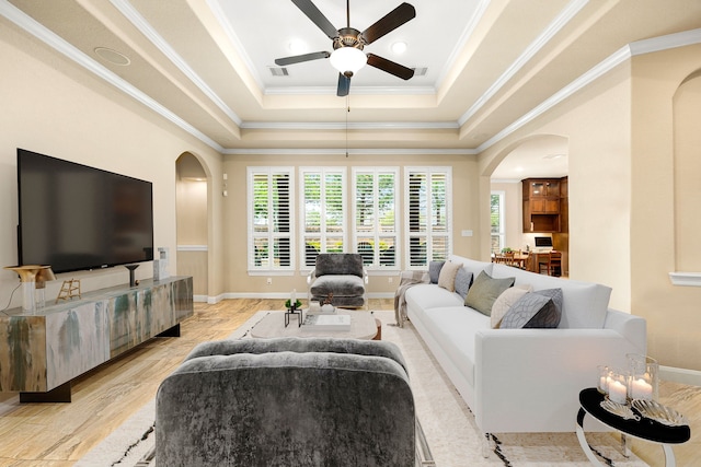 living room featuring arched walkways, a tray ceiling, a ceiling fan, ornamental molding, and baseboards