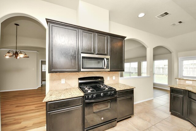 2614 Leopard Ct, Katy, TX 77449 - kitchen with black range with gas cooktop, stainless steel microwave, decorative backsplash, light stone counters, and baseboards