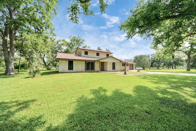 1417 Brigance Rd, Brazoria, TX 77422 - rear view of house featuring an attached garage, a lawn, concrete driveway, and metal roof