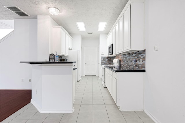 16106 Greenport Ln, Houston, TX 77084 - kitchen featuring white appliances, dark countertops, light tile patterned floors, white cabinets, and a textured ceiling