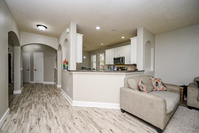 14720 Branchwest Dr, Houston, TX 77082 - kitchen featuring stainless steel microwave, arched walkways, light wood-style floors, white cabinets, and recessed lighting
