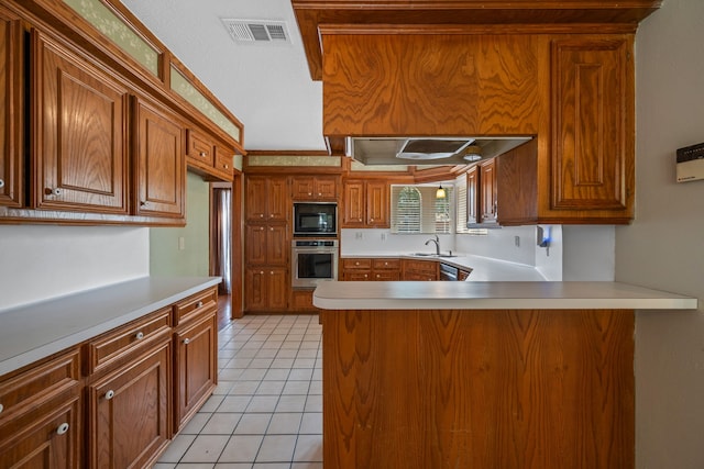 kitchen featuring oven, black microwave, a peninsula, brown cabinets, and light countertops