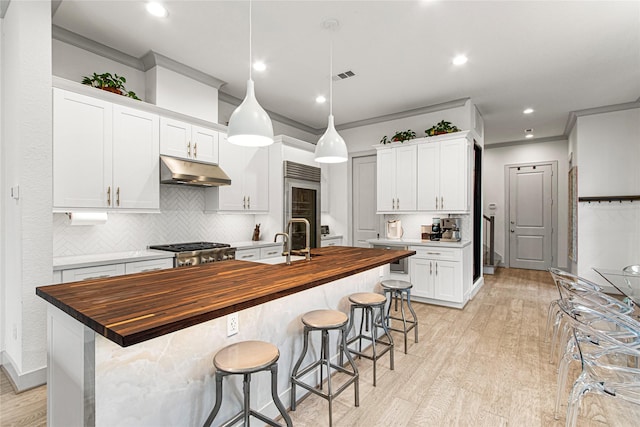 kitchen featuring wood counters, under cabinet range hood, ornamental molding, built in fridge, and backsplash