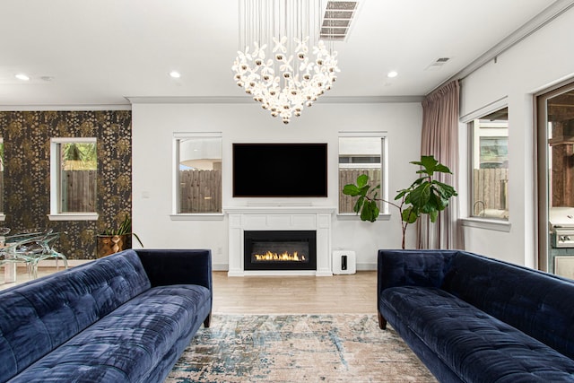 living area featuring crown molding, wood finished floors, a glass covered fireplace, a chandelier, and recessed lighting