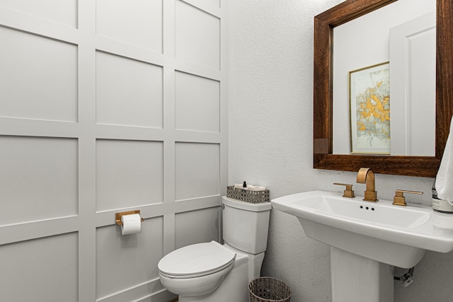 half bath featuring a textured wall, toilet, and a sink