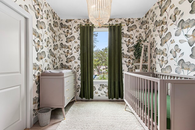 bedroom featuring wallpapered walls, a chandelier, multiple windows, a crib, and wood finished floors