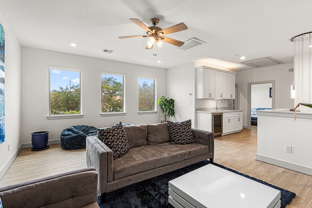 living area featuring attic access, light wood finished floors, wine cooler, ceiling fan, and baseboards