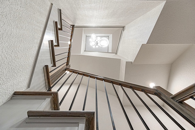 stairway with a textured wall, a chandelier, and a textured ceiling