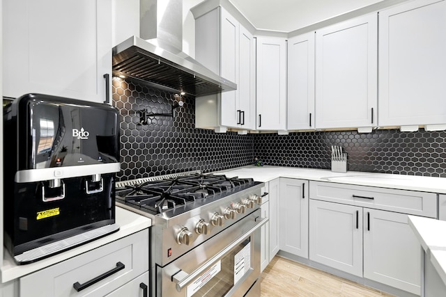 5209 Canal St, Houston, TX 77011 - kitchen featuring high end stainless steel range, wall chimney exhaust hood, light countertops, decorative backsplash, and light wood-style floors