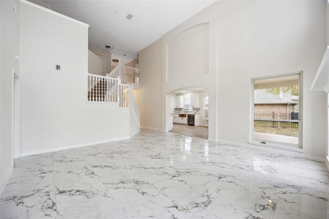 1910 Shark Ct, Crosby, TX 77532 - unfurnished living room featuring arched walkways, a towering ceiling, stairway, baseboards, and marble finish flooring