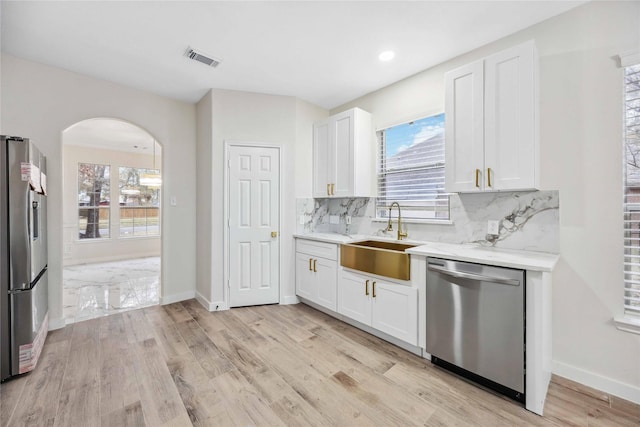 1910 Shark Ct, Crosby, TX 77532 - kitchen featuring appliances with stainless steel finishes, a sink, white cabinets, arched walkways, and decorative backsplash