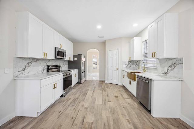 1910 Shark Ct, Crosby, TX 77532 - kitchen featuring stainless steel appliances, a sink, baseboards, arched walkways, and light wood finished floors