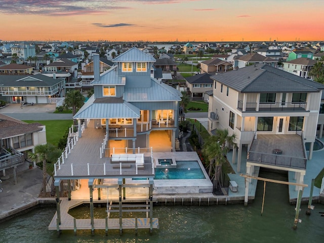 1311 Oahu Dr, Tiki Island, TX 77554 - back of property at dusk featuring a balcony, a water view, a residential view, metal roof, and a pool with connected hot tub