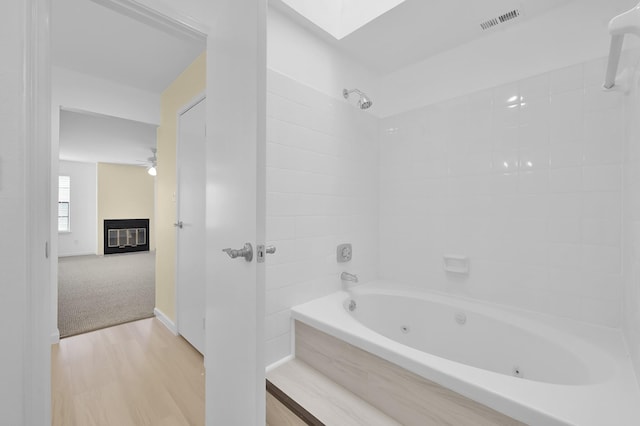 9850 Pagewood Ln Unit 1208, Houston, TX 77042 - bathroom featuring a glass covered fireplace, a combined bath / shower with jetted tub, wood finished floors, a skylight, and baseboards