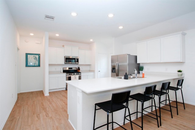 kitchen with appliances with stainless steel finishes, a kitchen breakfast bar, light wood-type flooring, a peninsula, and recessed lighting