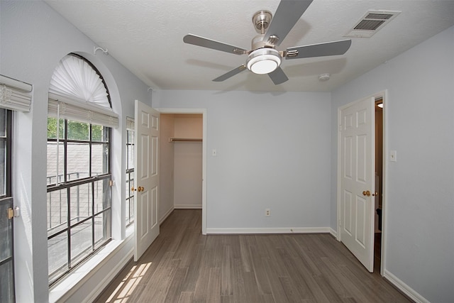 2030 Cutter Dr, League City, TX 77573 - unfurnished bedroom with wood finished floors, a walk in closet, baseboards, a ceiling fan, and a textured ceiling