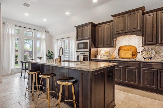 kitchen with appliances with stainless steel finishes, a sink, decorative backsplash, vaulted ceiling, and light stone counters
