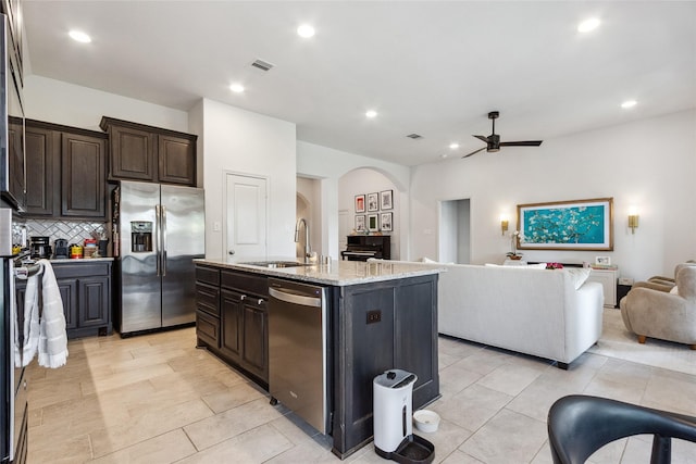 kitchen with stainless steel appliances, a sink, open floor plan, ceiling fan, and arched walkways