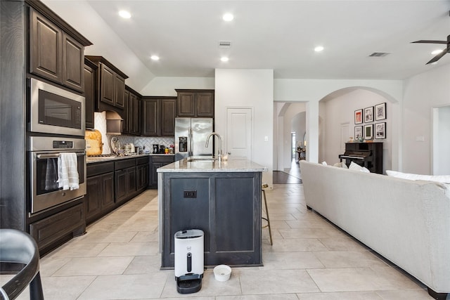 kitchen with appliances with stainless steel finishes, arched walkways, a sink, tasteful backsplash, and light stone countertops