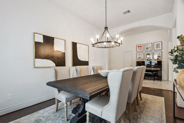 dining space with a chandelier, arched walkways, dark wood-style flooring, and baseboards