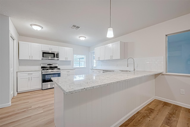 103 Anna St, Tomball, TX 77375 - kitchen featuring stainless steel appliances, a sink, light wood-style floors, a peninsula, and white cabinetry