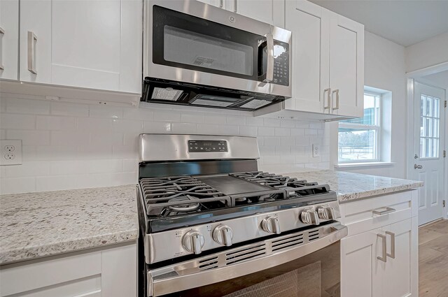 103 Anna St, Tomball, TX 77375 - kitchen with appliances with stainless steel finishes, white cabinetry, light wood-style flooring, tasteful backsplash, and light stone countertops