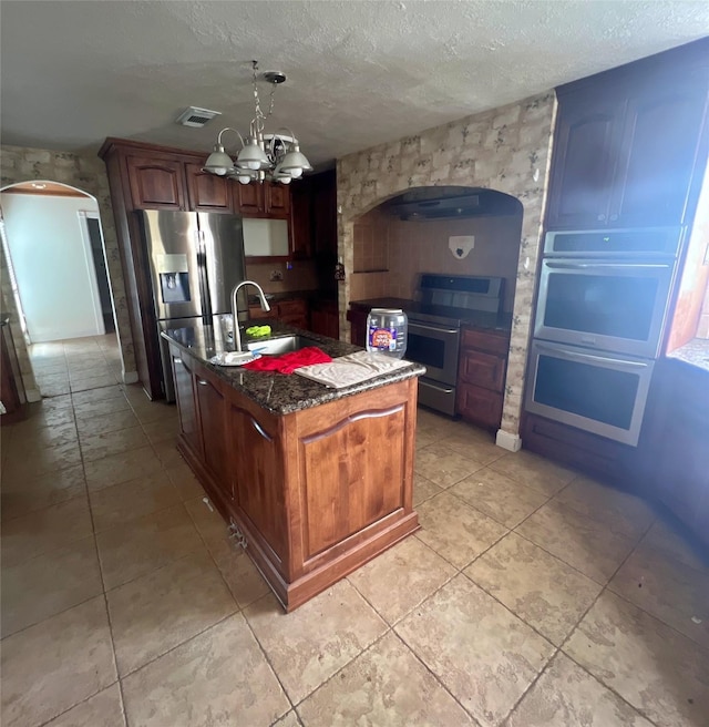 3811 Empress Ln, Richmond, TX 77406 - kitchen featuring a sink, a kitchen island with sink, a chandelier, appliances with stainless steel finishes, and dark stone countertops