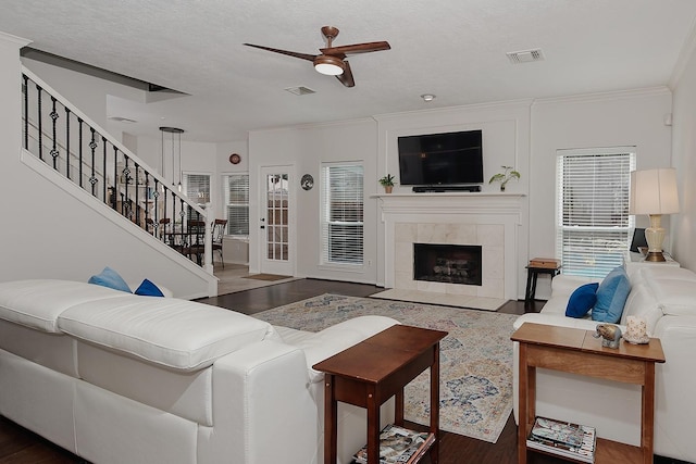 living room featuring a ceiling fan, stairway, wood finished floors, a tiled fireplace, and crown molding