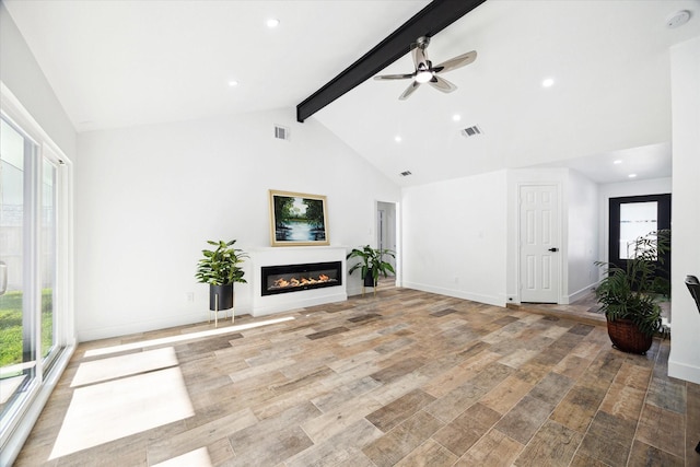 unfurnished living room featuring plenty of natural light, beam ceiling, a ceiling fan, a glass covered fireplace, and high vaulted ceiling