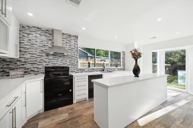 kitchen featuring black appliances, wall chimney exhaust hood, healthy amount of natural light, tasteful backsplash, and recessed lighting
