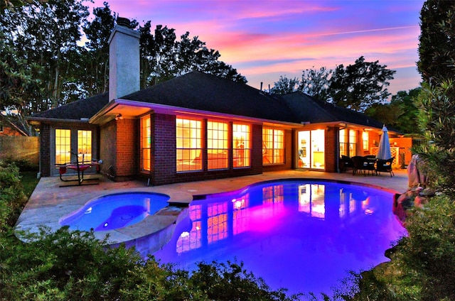 13702 Senca Park Dr, Houston, TX 77077 - back of house at dusk with french doors, a chimney, a patio, and a pool with connected hot tub