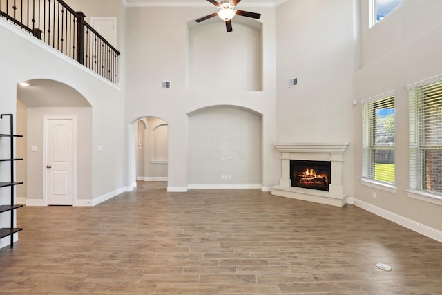 29407 Amber Meadows Ct, Katy, TX 77494 - unfurnished living room featuring a ceiling fan, arched walkways, wood finished floors, a lit fireplace, and ornamental molding
