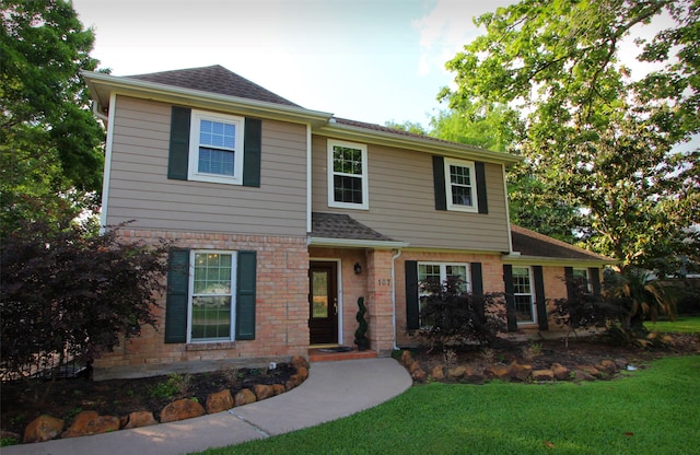 view of front of property featuring a front lawn, a shingled roof, and brick siding