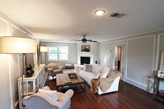 living area featuring a decorative wall, a textured ceiling, dark wood-type flooring, a fireplace, and ceiling fan