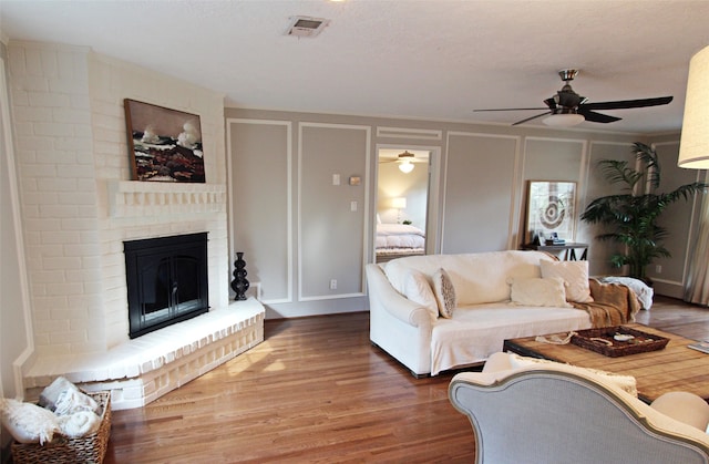 living area with a decorative wall, a ceiling fan, wood finished floors, and a fireplace