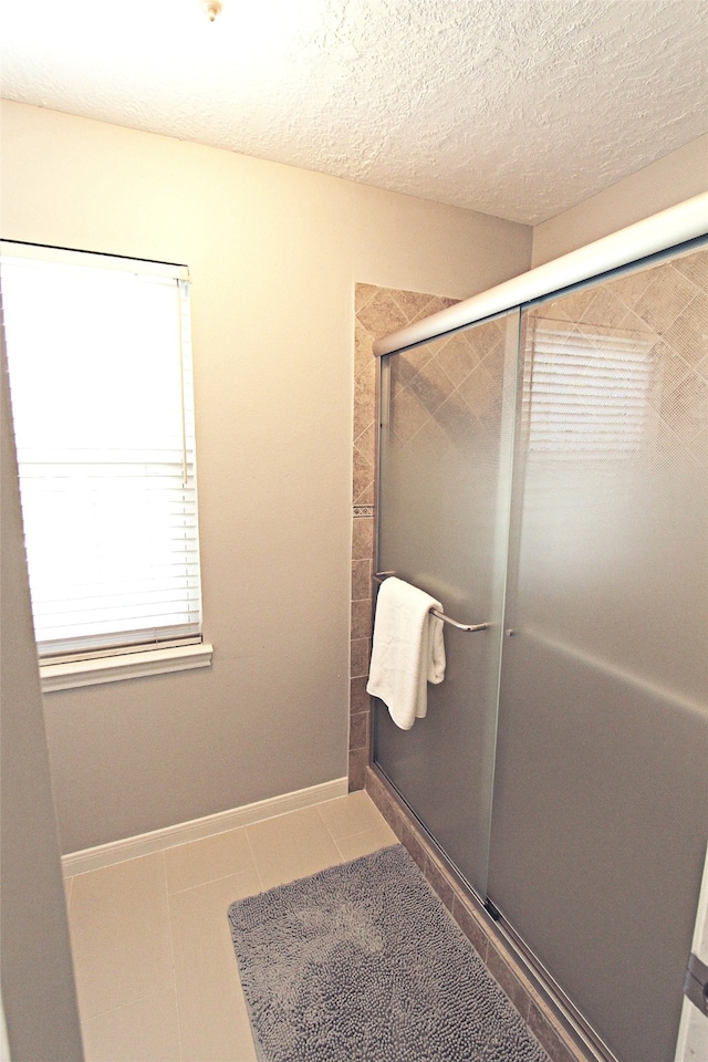 bathroom featuring a shower stall, baseboards, tile patterned flooring, and a textured ceiling