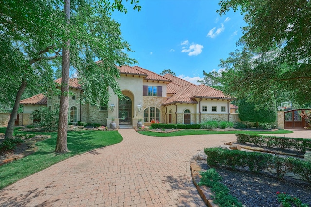 mediterranean / spanish-style house featuring stone siding, stucco siding, curved driveway, and a tile roof