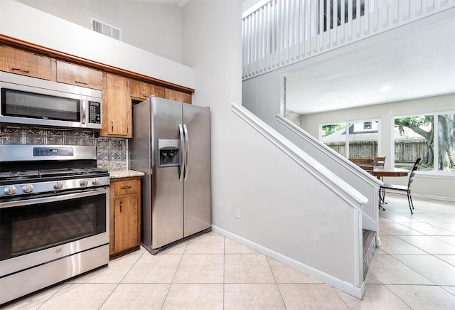 22331 Unicorns Horn Ln, Katy, TX 77449 - kitchen with stainless steel appliances, brown cabinetry, light tile patterned floors, a towering ceiling, and tasteful backsplash