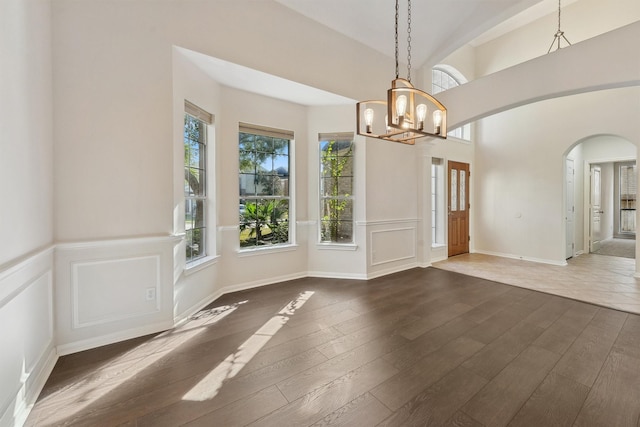 unfurnished dining area with hardwood / wood-style flooring, a chandelier, arched walkways, wainscoting, and a decorative wall