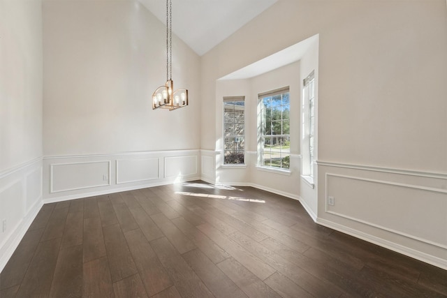 unfurnished dining area with lofted ceiling, a chandelier, dark wood-style floors, a wainscoted wall, and a decorative wall