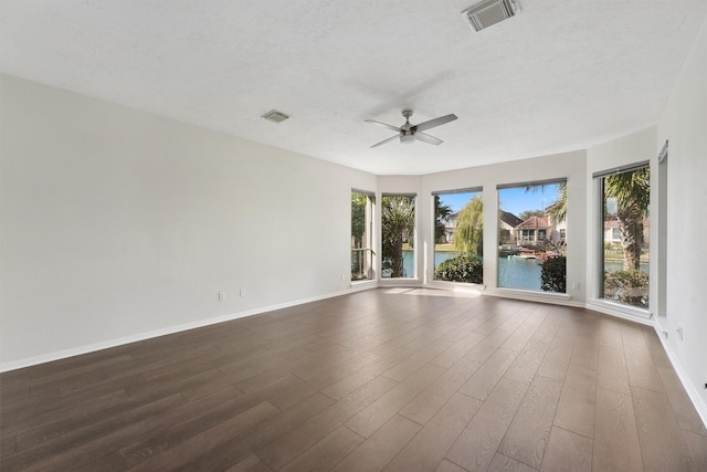 empty room featuring ceiling fan, dark wood-style flooring, baseboards, a water view, and a textured ceiling