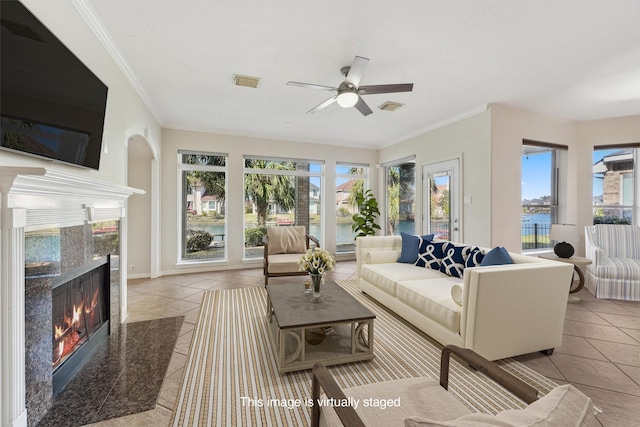 tiled living room with healthy amount of natural light, a fireplace, a ceiling fan, ornamental molding, and a water view