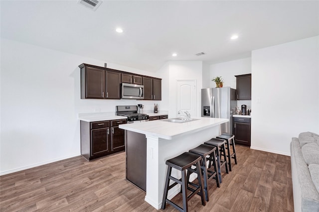 21614 Gusto Glen Ln, Katy, TX 77449 - kitchen featuring stainless steel appliances, a sink, dark brown cabinets, a kitchen bar, and light wood finished floors