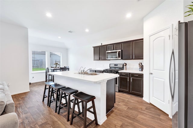 21614 Gusto Glen Ln, Katy, TX 77449 - kitchen featuring stainless steel appliances, a sink, a breakfast bar, dark brown cabinets, and light wood-style flooring
