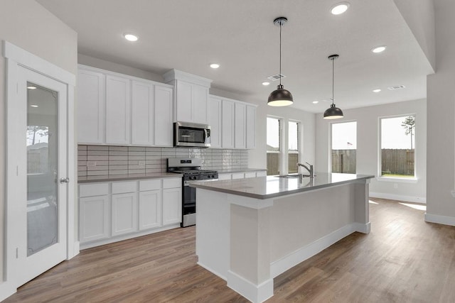 21611 Elmheart Dr, New Caney, TX 77357 - kitchen with stainless steel appliances, backsplash, light wood finished floors, white cabinets, and an island with sink