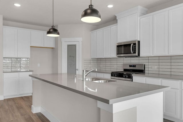 21611 Elmheart Dr, New Caney, TX 77357 - kitchen with appliances with stainless steel finishes, light wood-style floors, a center island with sink, decorative backsplash, and white cabinetry