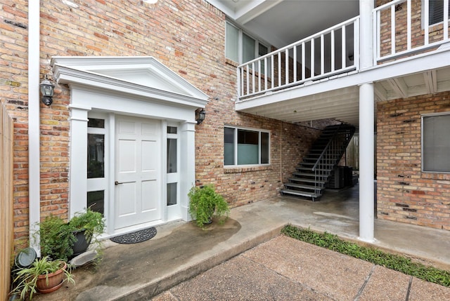 entrance to property with brick siding, a balcony, and central air condition unit