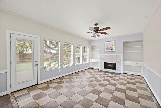 unfurnished living room with ornamental molding, baseboards, a ceiling fan, built in shelves, and a stone fireplace