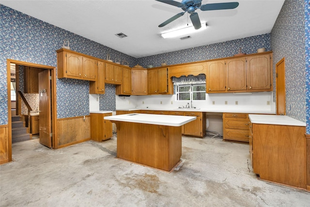 24614 Spruce, Huntsville, TX 77320 - kitchen featuring wallpapered walls, a kitchen island, a ceiling fan, brown cabinetry, and concrete flooring